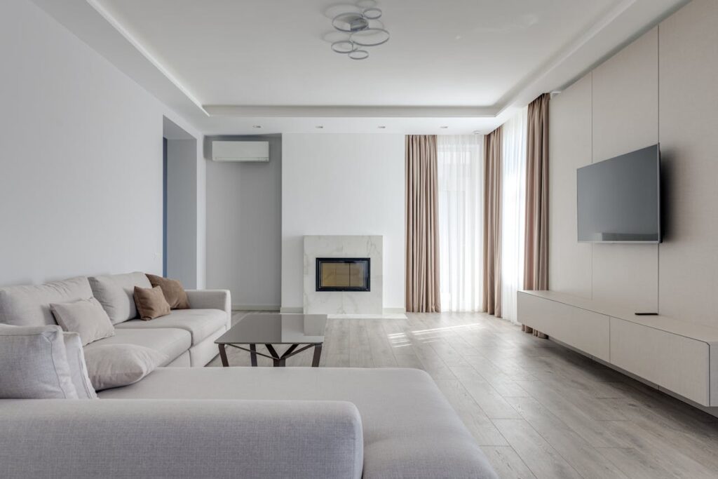 pexels-photo-5998138 Interior of light living room in pastel colors with comfortable couch near glass table and TV set